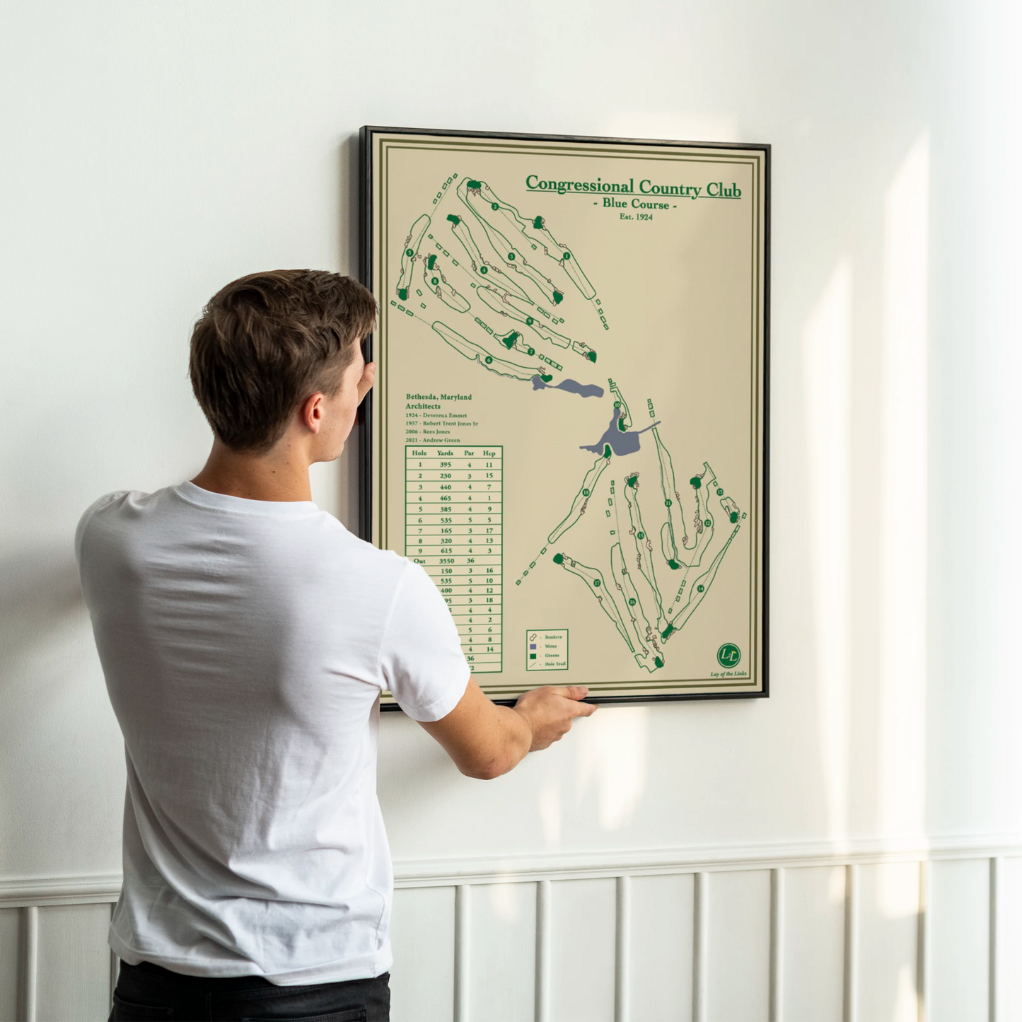 Man looking at a framed course map of the Blue Course at Congressional Country Club on a white wall.