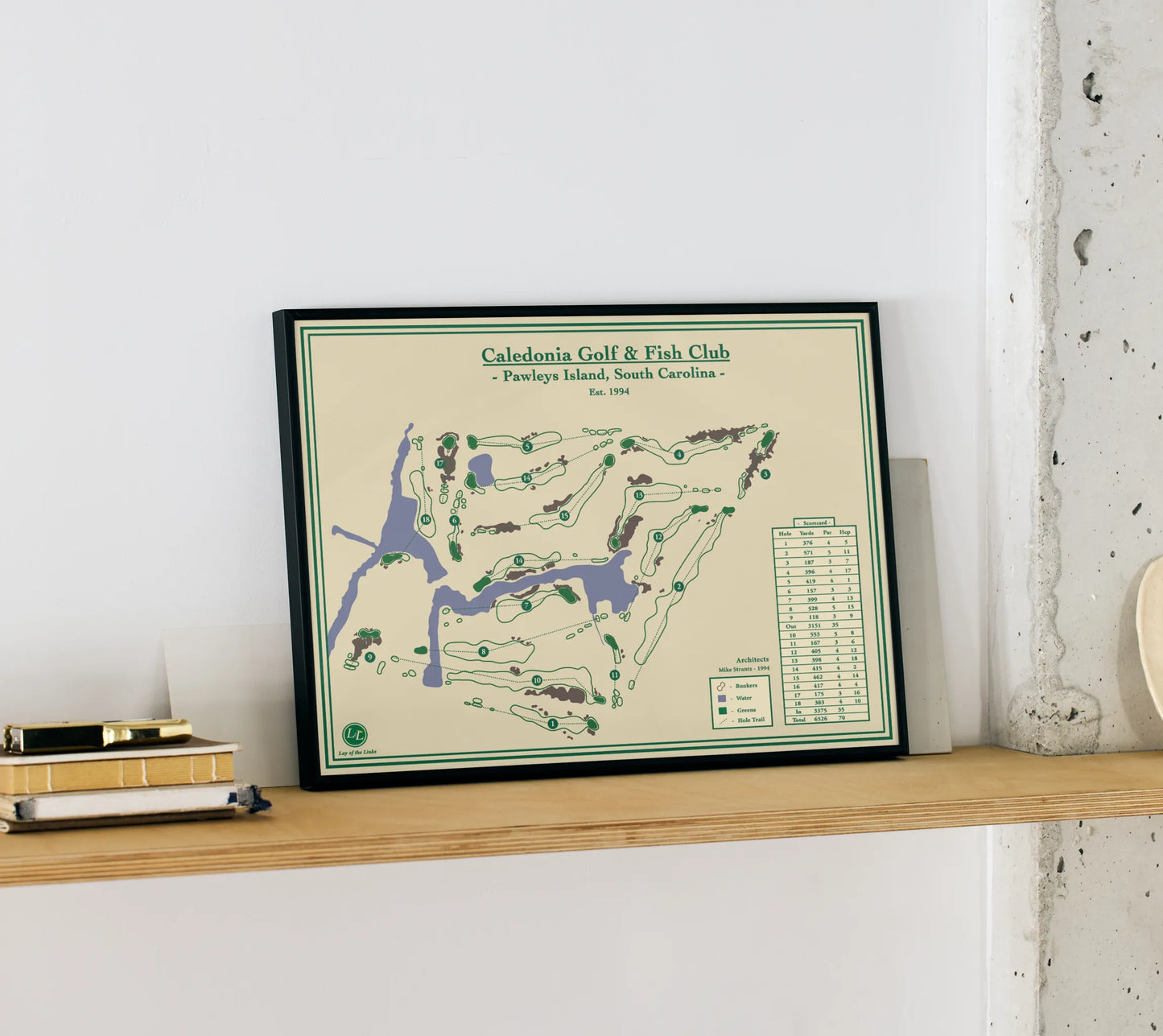 Framed golf print of Caledonia Golf & Fish Club on a wooden shelf.