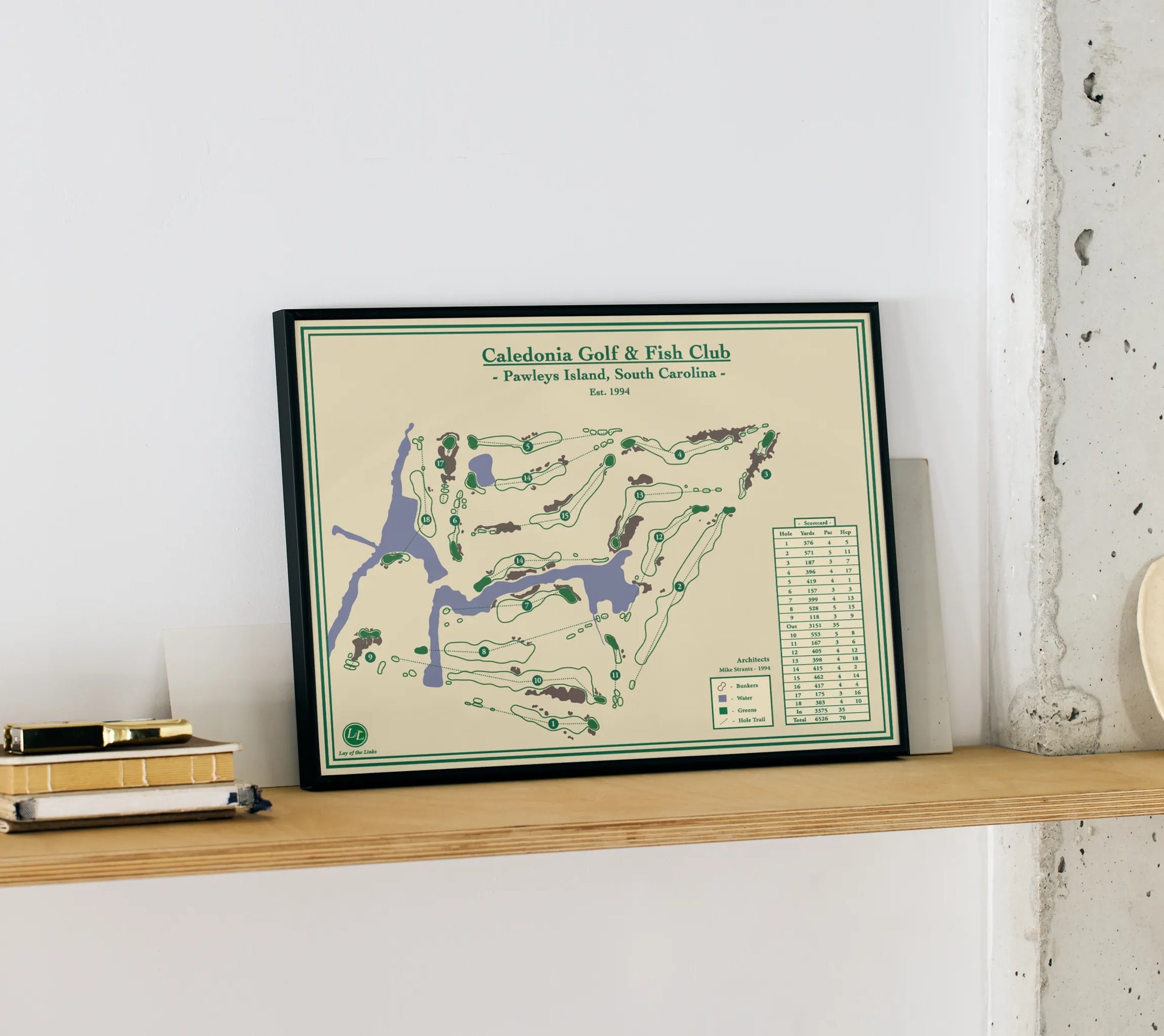 Framed golf print of Caledonia Golf & Fish Club on a wooden shelf.