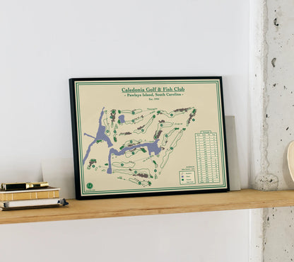 Framed golf print of Caledonia Golf & Fish Club on a wooden shelf.