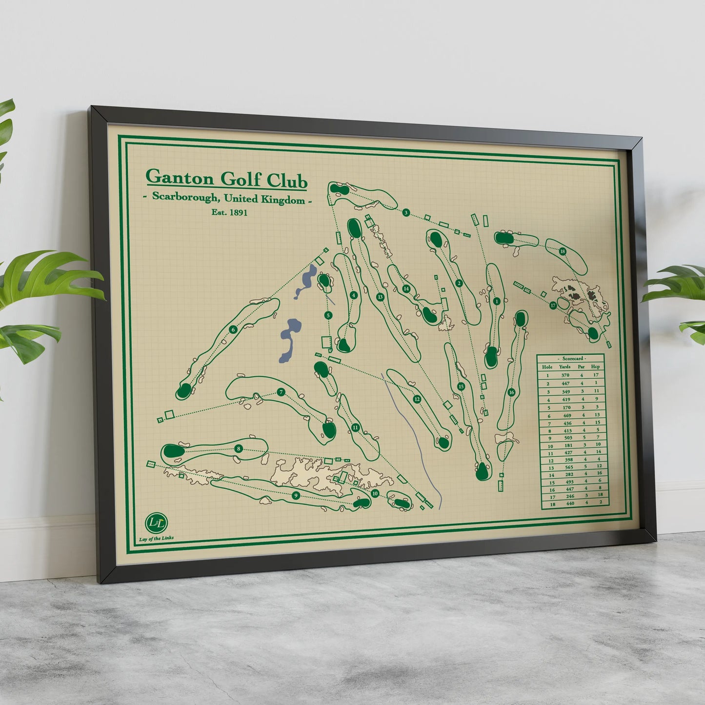 A framed golf course map print for Ganton Golf Club, Scarborough, United Kingdom, featuring a cream background with green course markings and a black frame, styled on a marble surface against a white wall with green leaves at the sides.
