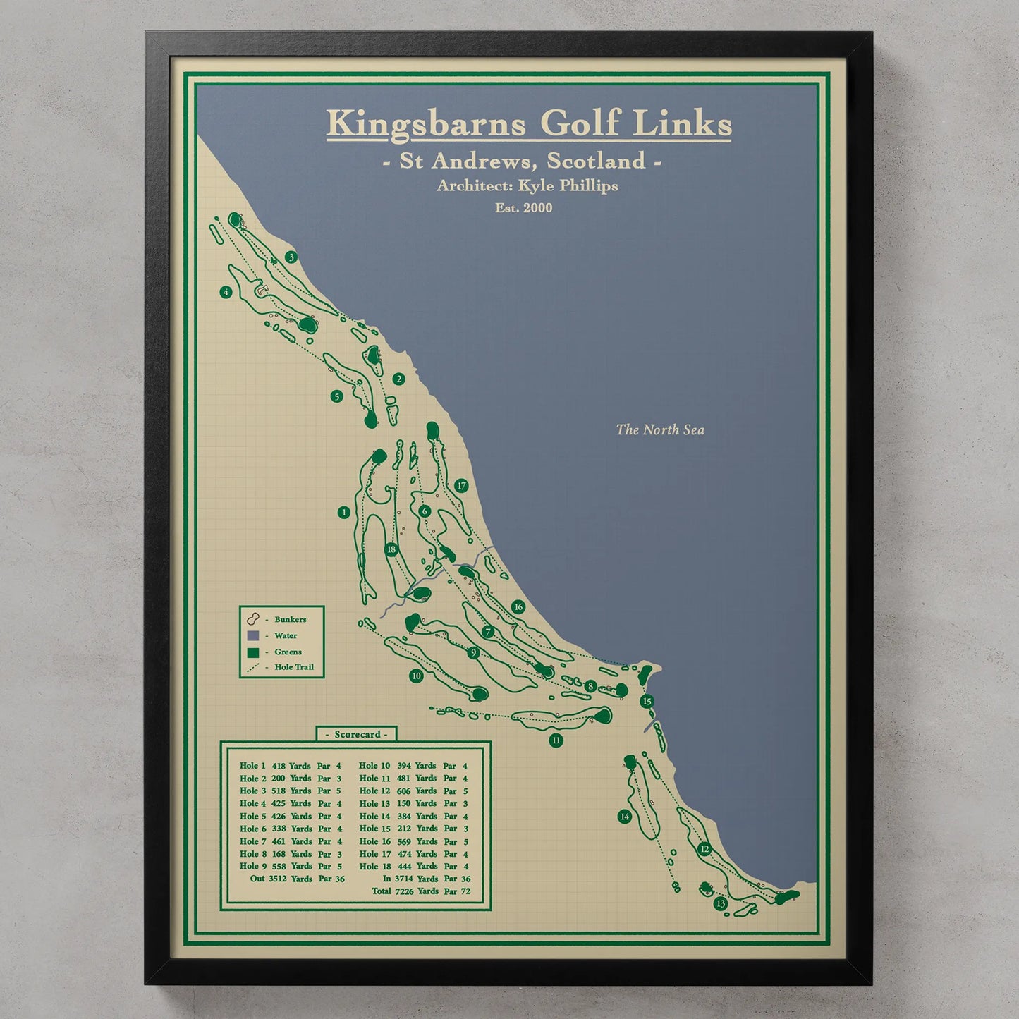 A framed golf course map print titled 'Kingsbarns Golf Links' showing the course layout in St Andrews, Scotland, with green tee marks on a beige and blue map background, enclosed in a black frame against a light gray wall.